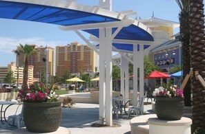 An outdoor patio area with tables and chairs, surrounded by potted plants and umbrellas.