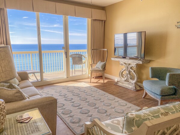 A living room with a large window overlooking the ocean, a television, and a comfortable seating area.