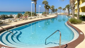 Une piscine avec des chaises longues et des palmiers, une jetée en arrière-plan et un ciel bleu dégagé.