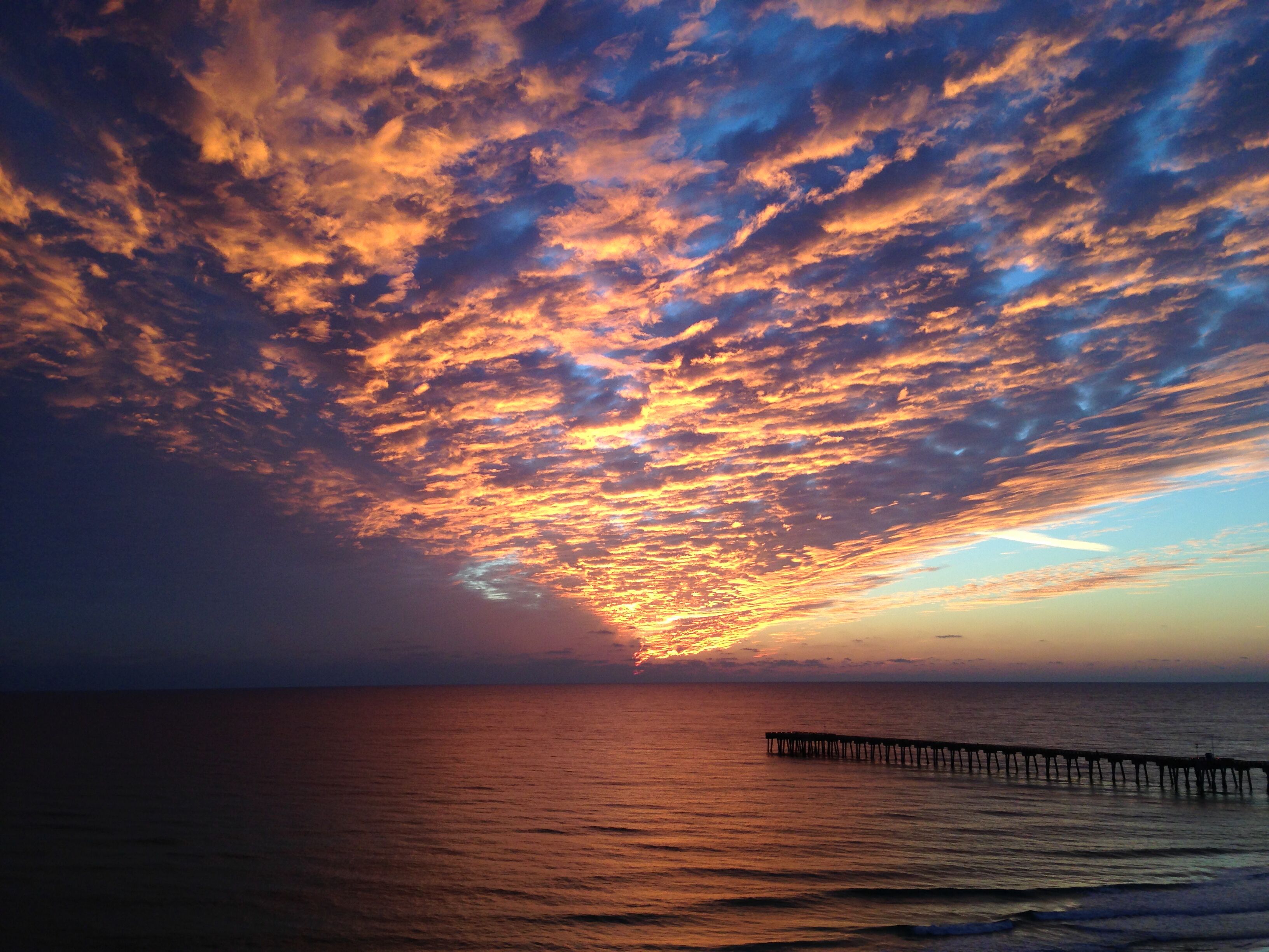 Ein Sonnenuntergang über einem ruhigen Meer mit einem Steg, der sich ins Wasser erstreckt.