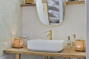Une salle de bain avec un lavabo blanc, un robinet doré et deux porte-bougies en osier.