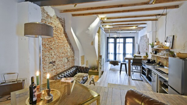 Un espacio habitable tipo loft con paredes de ladrillo visto, techo de madera, un sofá de cuero, zona de comedor y cocina.