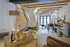 A loft-style living space with exposed brick walls, a wooden ceiling, a leather sofa, a dining area, and a kitchen. - Big appartement in city centre Amsterdam with 2 bedrooms all highlights 4 walk (Amsterdam)