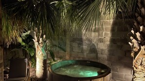 Ein Whirlpool in einem überdachten Außenbereich mit Backsteinwand und Palmen.
