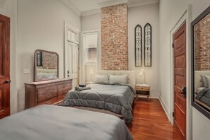 A bedroom with a brick accent wall, a large bed, a dresser, a nightstand, and a mirror. - Upscale and Historic, 2 blocks to Streetcar, 4 to French Quarter, 6 to Frenchmen (New Orleans)