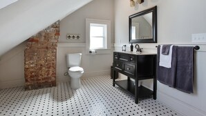 Ein Badezimmer mit weißer Toilette, einem schwarz-weißen Bodenbelag, einem schwarzen Waschtisch mit Spiegel und einem Handtuchhalter.