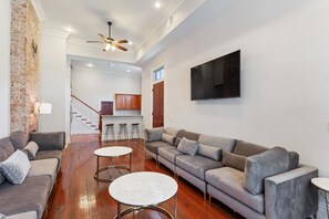 Uma sala de estar moderna com um sofá, duas mesas redondas, um ventilador de teto e uma TV fixada na parede.