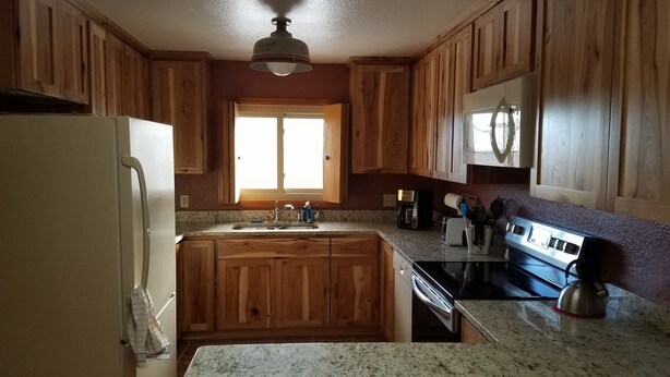Una cocina con armarios de madera, encimera de granito, estufa de acero inoxidable y refrigerador.