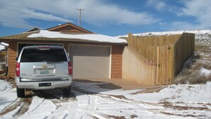 Una casa en una zona residencial con garaje, valla de madera y entrada cubierta de nieve.