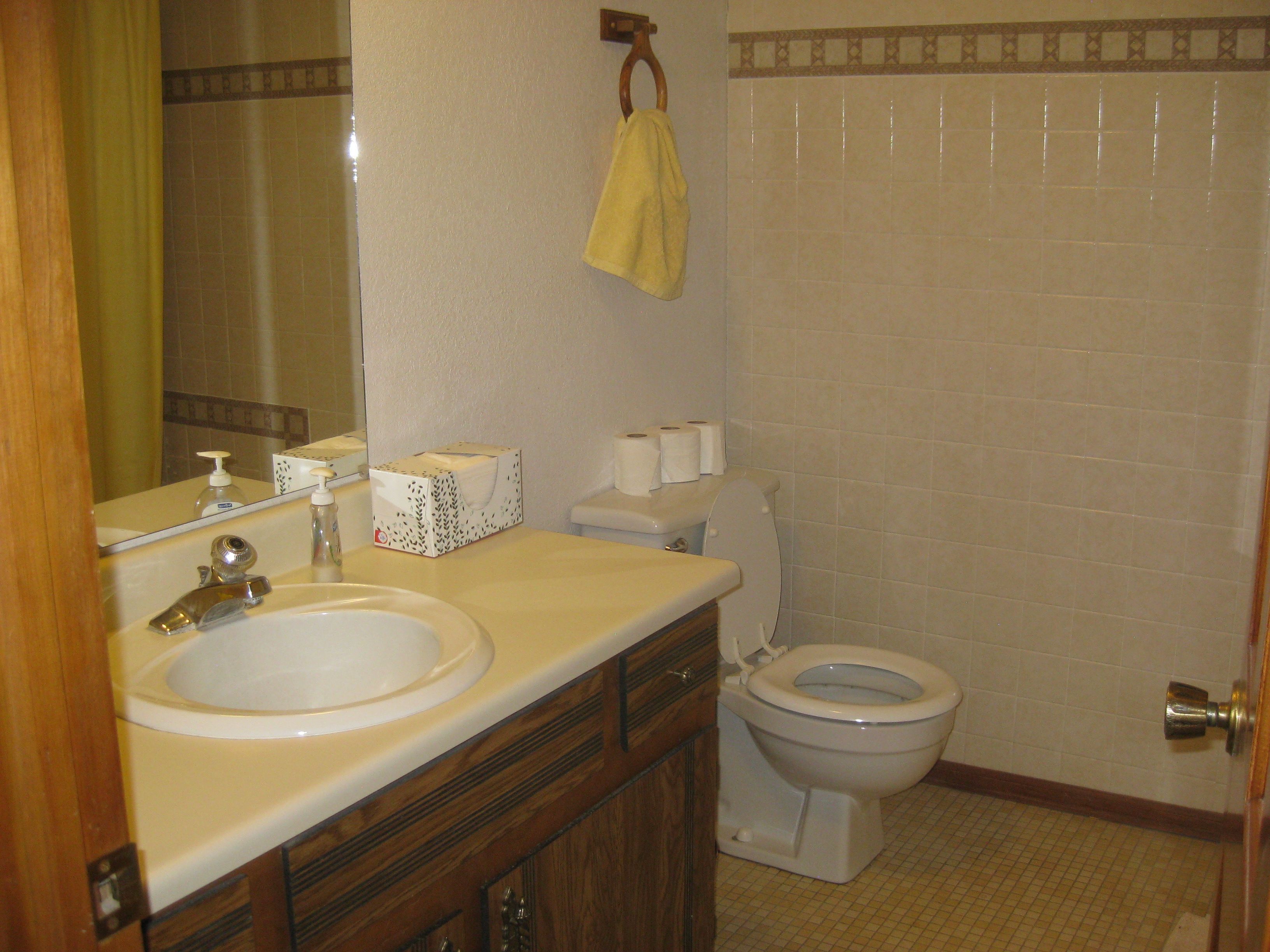 A bathroom with a sink, mirror, toilet, and a towel hanging on the wall.