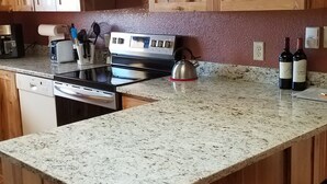 Una cocina con armarios de madera, encimera de granito, hervidor, tostadora y botellas de vino.