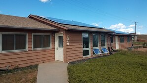 Una edificación de un piso con revestimiento marrón, identificada con el número 2359, que cuenta con ventanas amplias y un visible conjunto de paneles solares en el techo.