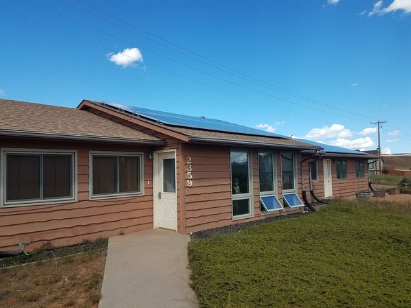 Um edifício térreo com revestimento marrom, número 2359, com grandes janelas e um conjunto de painéis solares visíveis no telhado.