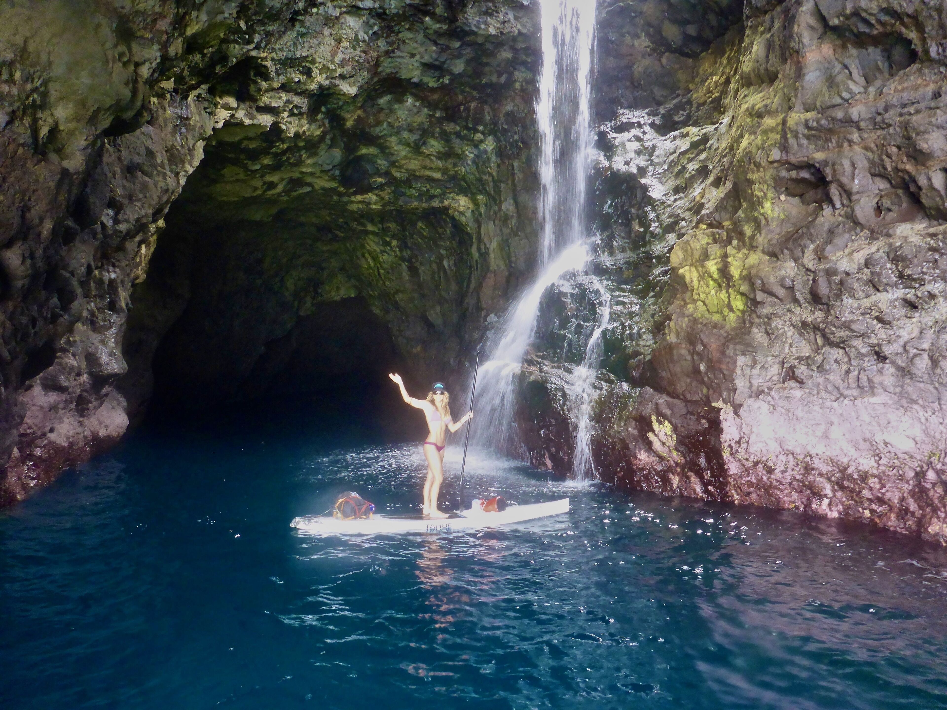 Una persona de pie sobre una tabla de surf dentro de una cueva con una cascada.