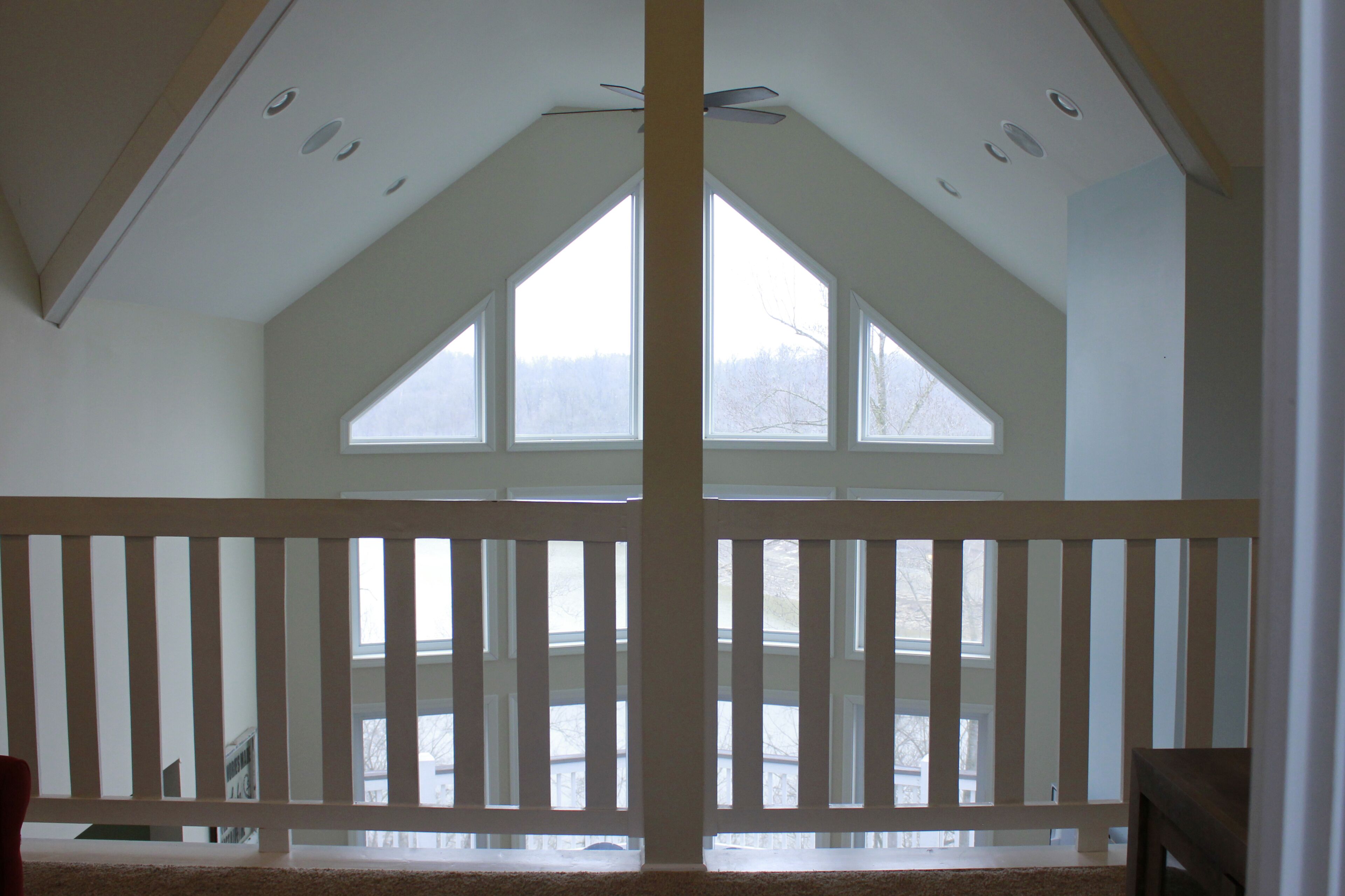 Une pièce avec un plafond haut, de grandes fenêtres et une balustrade en bois.