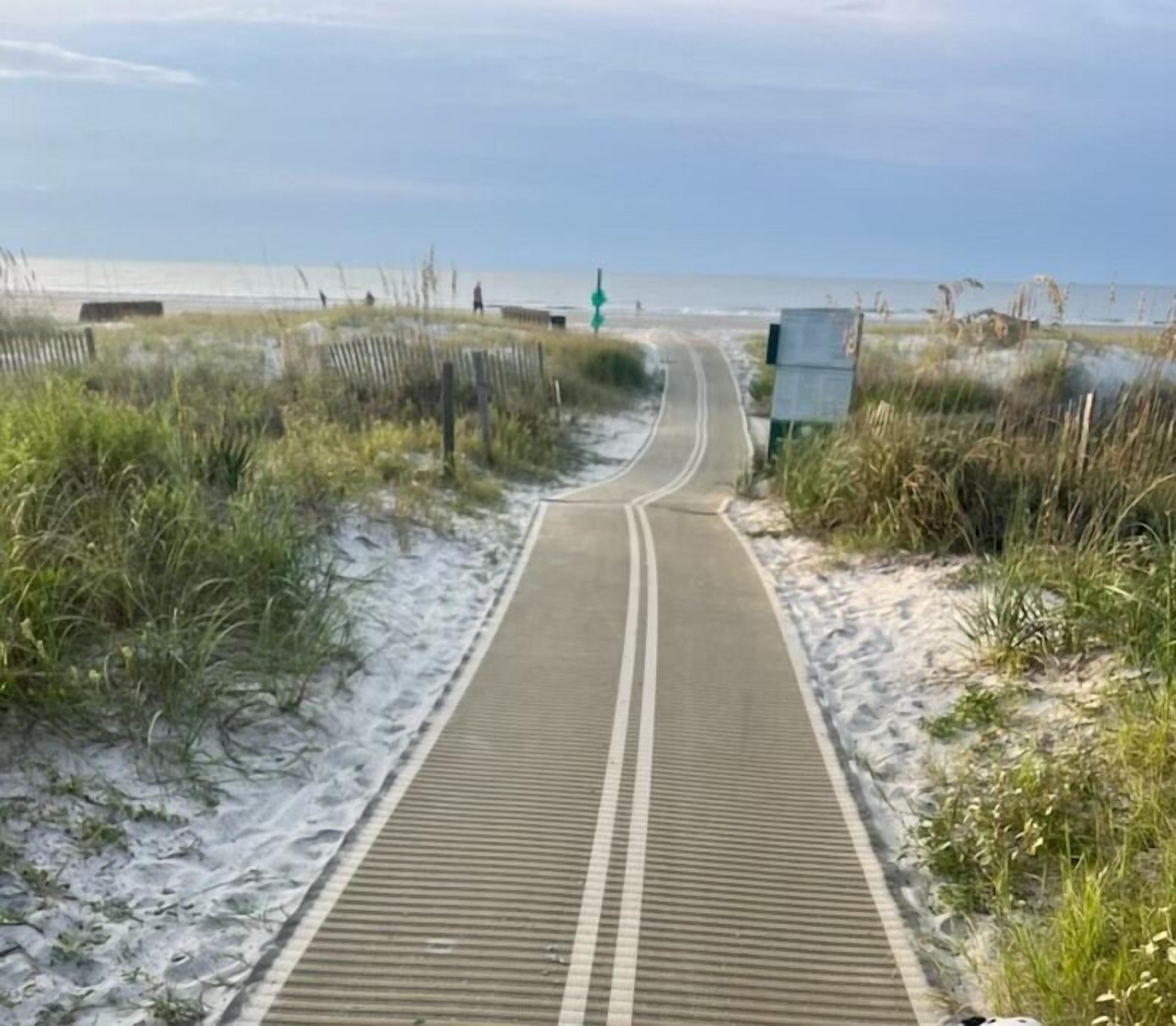 A pathway leading to a beach with a wooden boardwalk and sand dunes.