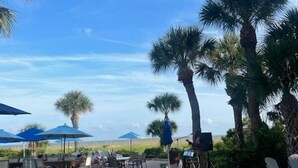 An outdoor patio area with seating arrangements, palm trees, and umbrellas. - 3BR 2.5 BA, short walk or 5 min bike to beach w/ cart, chairs, pools, sm. dog (Hilton Head Island)