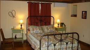 A bedroom with a wooden ceiling, a bed with a metal frame, two bedside tables with lamps, a chair, and a wall decoration.
