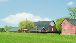 A red barn with a green roof, a white silo, and a wooden fence in a grassy field.
