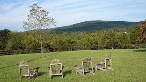 Three Adirondack chairs on a grassy field with a mountain in the background.