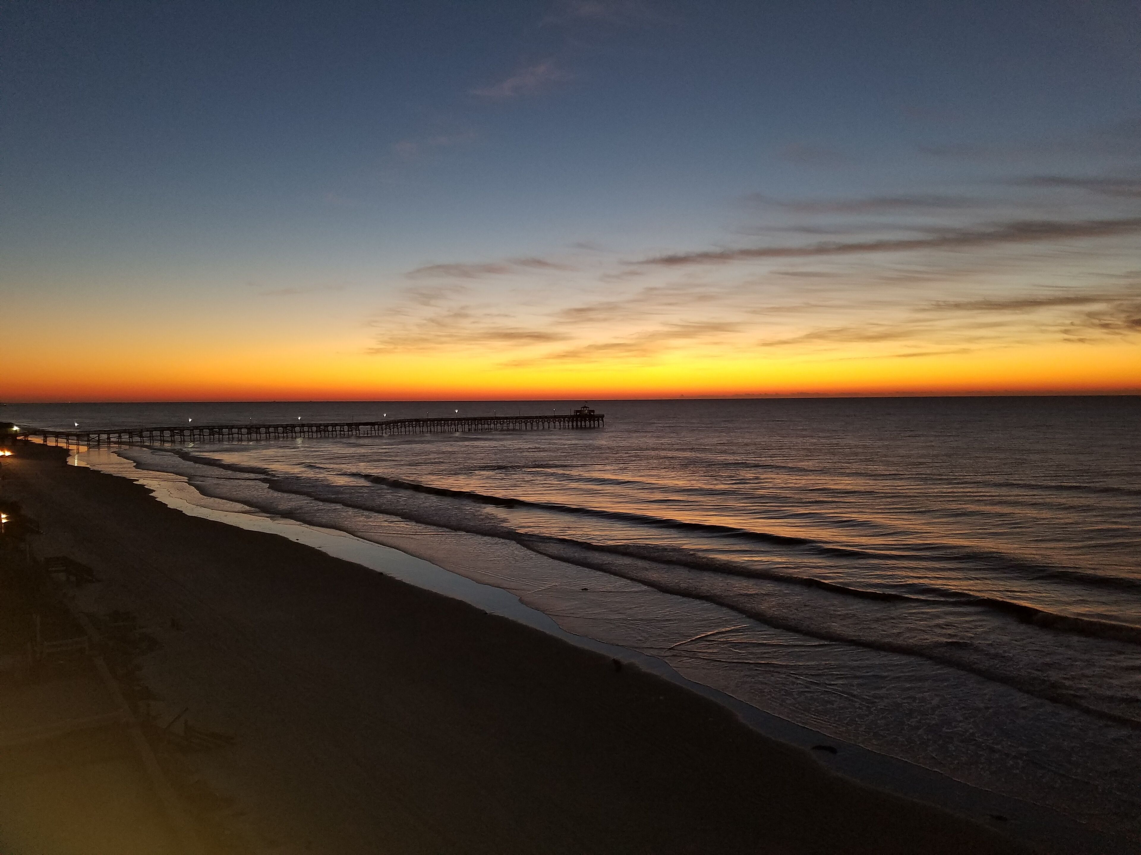 Une plage avec une jetée en bois qui s’avance dans l’océan au coucher du soleil.