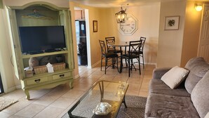 A living room with a television, a dining table with chairs, a sofa, and a decorative clock on the wall.