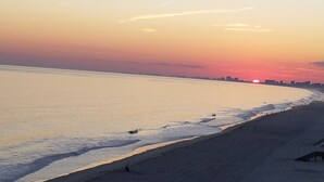 A beach with a sunset, a sandy shore, and a distant city skyline.