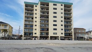 A multi-story hotel with balconies, a beach view, and a sandy ground in front.