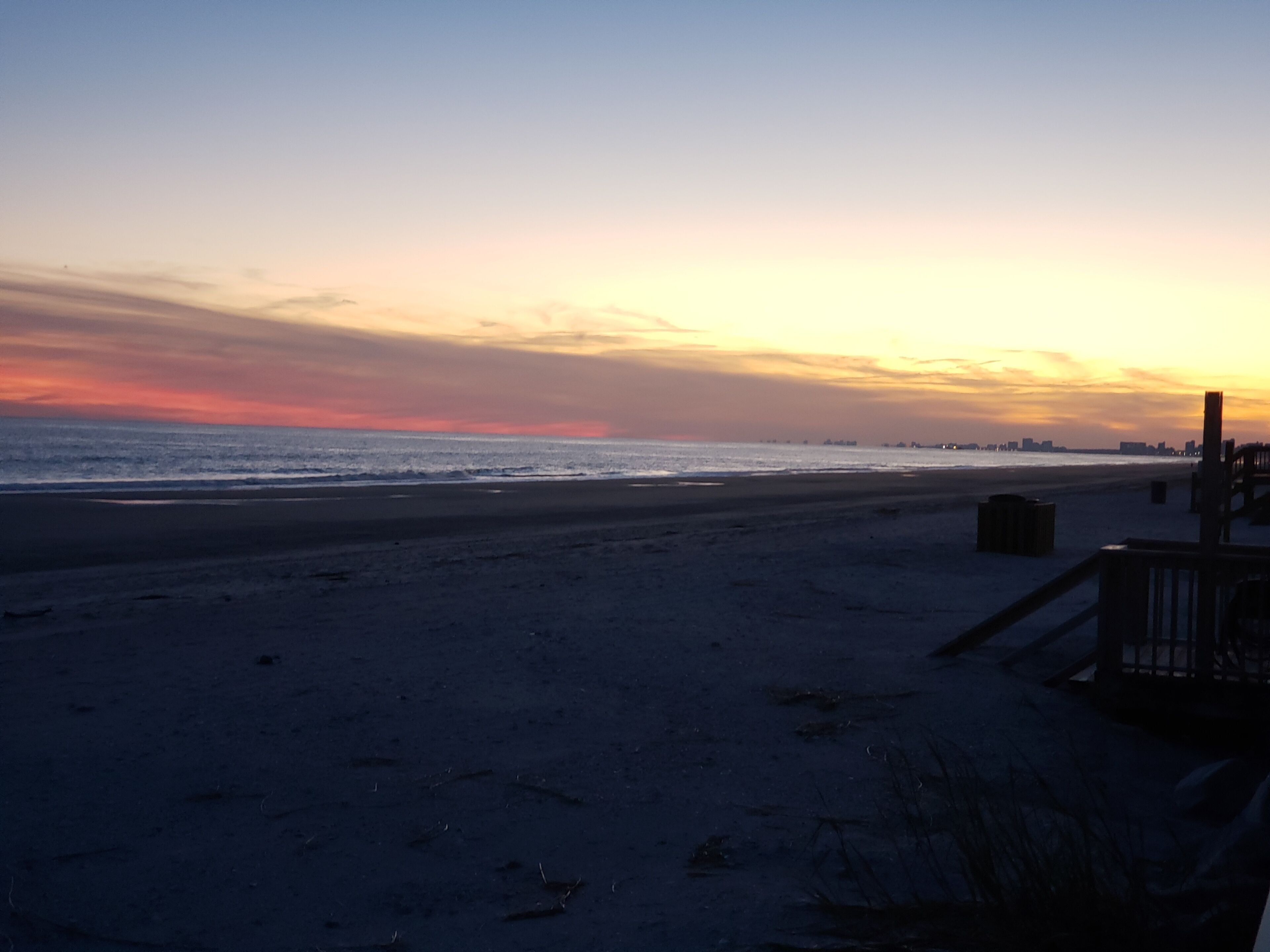 A beach with a wooden walkway and a railing on the right.