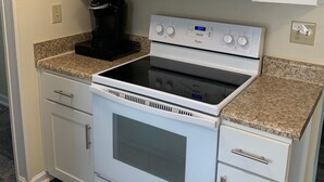 Une cuisine avec des meubles blancs, un four à micro-ondes, une cuisinière et une machine à café.