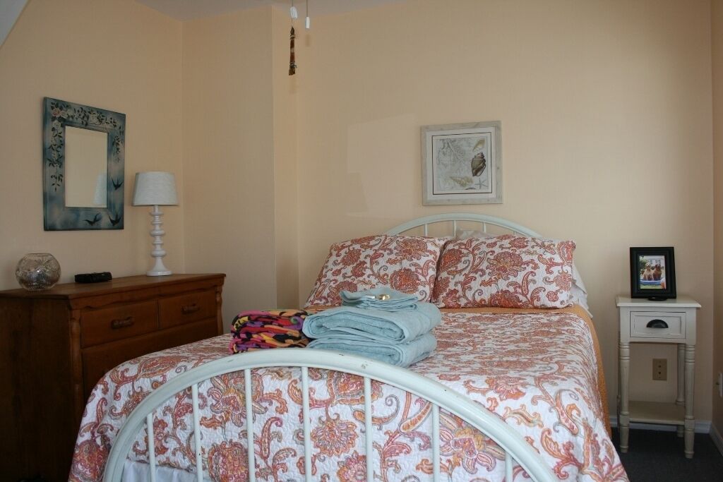 Une chambre à coucher comprenant un lit, une commode, une table de chevet et un mur orné de deux tableaux encadrés.