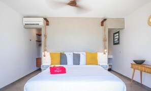 Une chambre d’hôtel comprenant un lit, une table de chevet, un climatiseur fixé au mur et une petite table d’appoint en bois avec un bol.