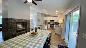 A modern kitchen with a stone fireplace, a dining area with a checkered tablecloth, and a view of the backyard through a sliding glass door. - Narragansett R.I. 5 Bedrooms, 3 full bathrooms, central air on cul-de-sac (Narragansett)