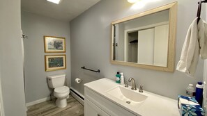 A bathroom with a toilet, sink, and mirror. There are framed pictures on the wall and a towel hanging on the wall. - Narragansett R.I. 5 Bedrooms, 3 full bathrooms, central air on cul-de-sac (Narragansett)
