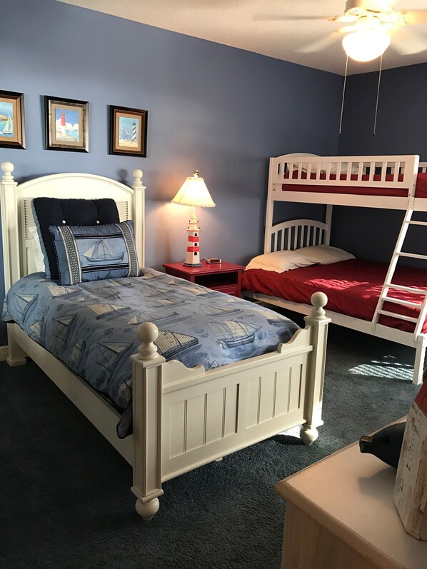 Un dormitorio con literas, una cama individual con colcha estampada, una mesita de noche con lámpara y cuadros en la pared.