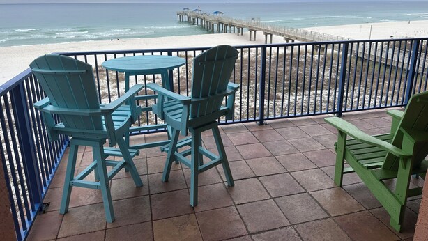 Eine Terrasse mit zwei Stühlen und einem Tisch, mit Blick auf einen Strand und einen Steg.
