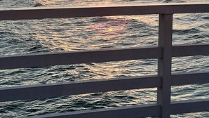 Ein Strand mit Sonnenuntergang, Meereswellen und Gebäuden im Hintergrund.