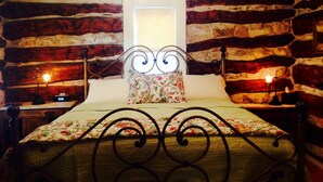 Una cama con un cojín floral y un cabecero de diseño único. La habitación tiene una pared de piedra rústica y una ventana pequeña.