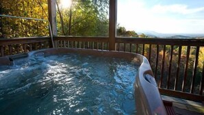 Un bain à remous sur une terrasse en bois, avec vue sur les arbres et les montagnes.