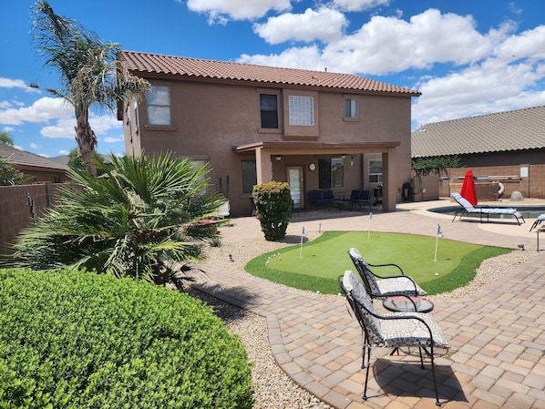 A two-story house with a patio area featuring a pool, outdoor seating, and a well-maintained lawn.