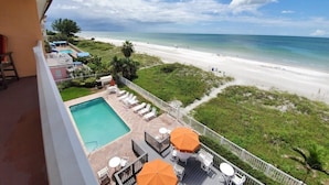 Uma varanda com vista para a praia, uma piscina e área de estar ao ar livre.