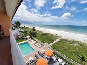 A balcony with a view of a beach, a swimming pool, and outdoor seating.