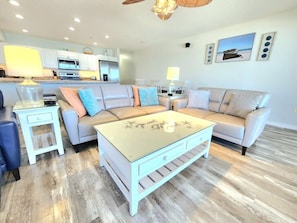 A living room with a sofa, a coffee table, a side table, and a kitchen in the background.