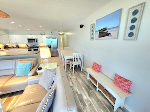 A modern kitchen with white cabinets, a dining area with a white table and chairs, a sofa with patterned cushions, and a bench with red cushions.