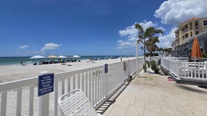 Uma passarela à beira-mar com cerca branca, guarda-sóis e uma placa indicando para colocar toalhas nas cadeiras e devolvê-las.