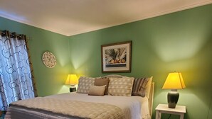 Une chambre à coucher avec un grand lit, deux tables de chevet avec des lampes, un élément décoratif mural et une fenêtre avec des rideaux à motifs.