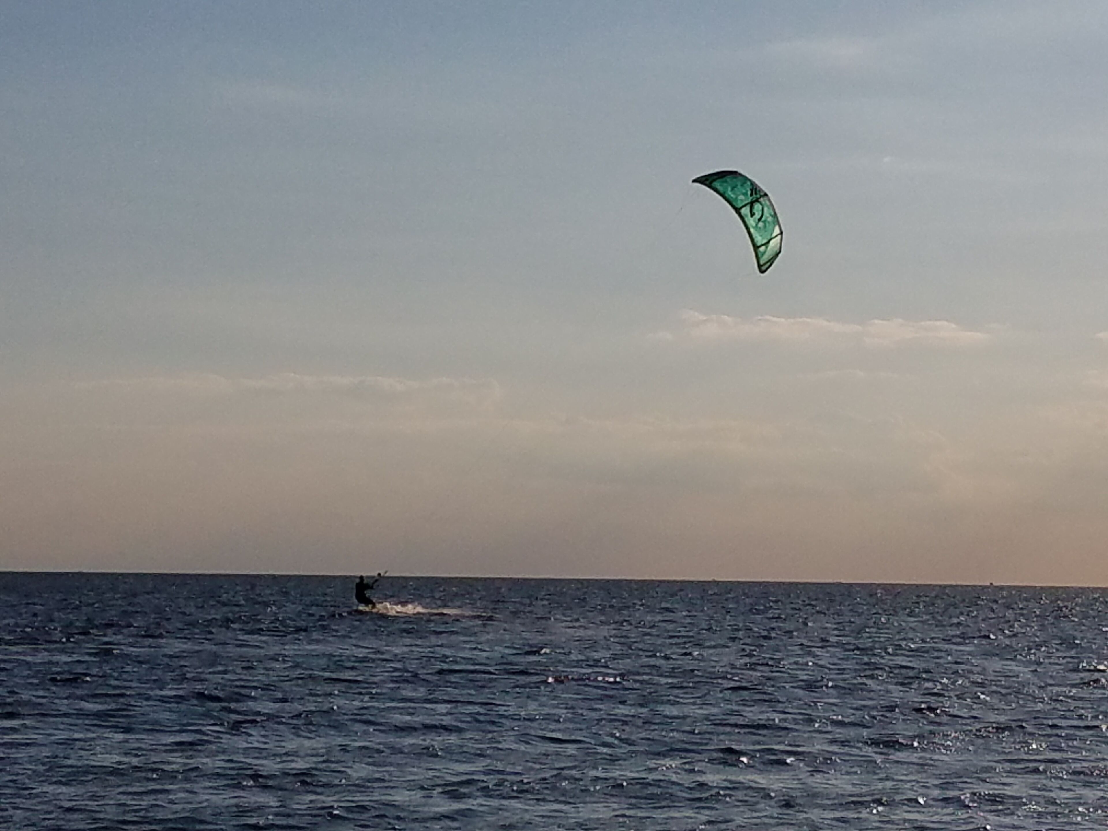 Una persona practica windsurf sobre un cuerpo de agua, usando una cometa verde.