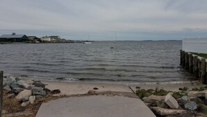 Une vue sur le front de mer, avec une promenade en béton menant à l’eau, une côte rocheuse et une vue lointaine sur des bâtiments et une jetée.