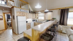 A kitchen with wooden cabinets, a white refrigerator, a microwave, and a bar area with stools.