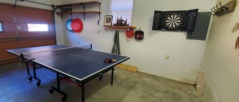A ping pong table in a room with a dartboard, a framed picture, and a window.